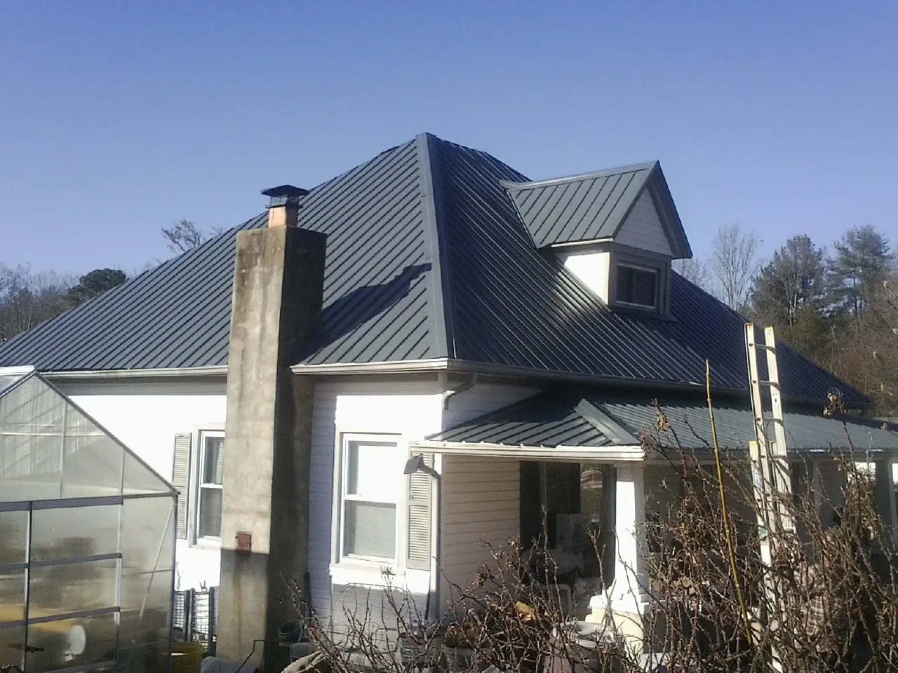 Dark blue standing seam metal roof on a white farmhouse with dormer — Slate & Tile Roof Repair by Roofing Brothers in Maple Heights