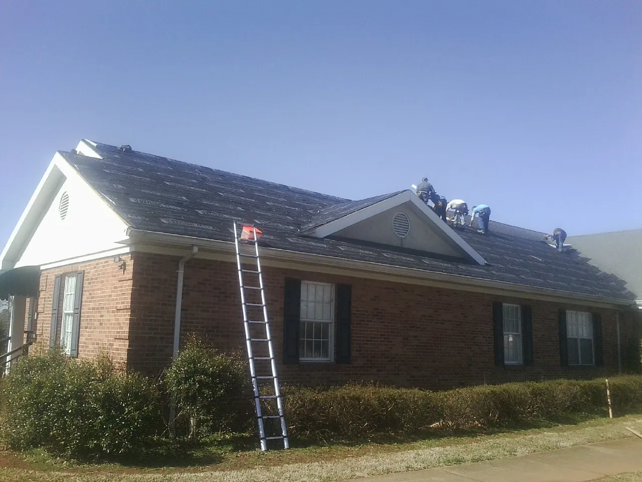 Crew tearing shingles off a brick ranch roof with a ladder set — Emergency Roof Repair work by our crew in Maple Heights