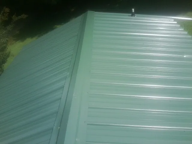 New green metal panels meeting at the ridge of a roof — Flat Roof Repair work by our crew in Maple Heights