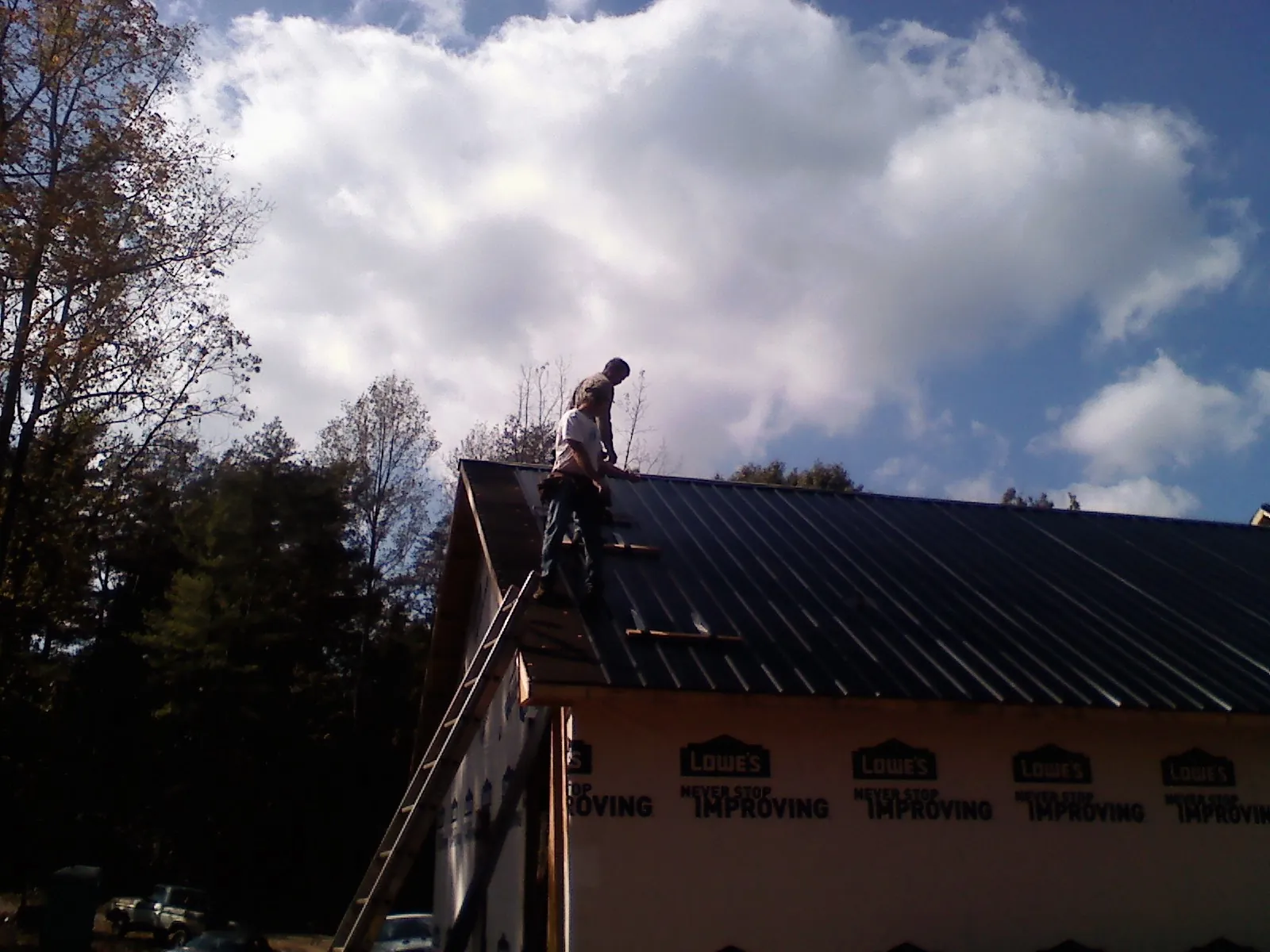 Roofer fastening dark metal panels high against a cloudy sky, from a Roof Inspection job in Maple Heights