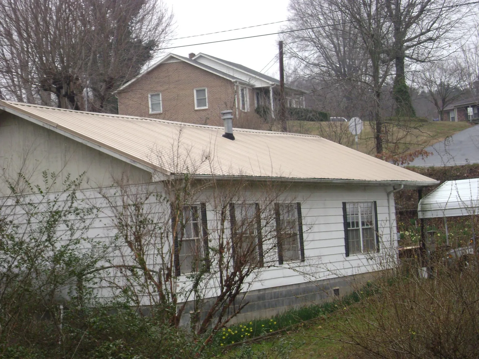Tan metal roof on a white sided house set into a hillside — Commercial Roofing by Roofing Brothers in Maple Heights